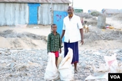 Ibrahim Hassan, with his son, stands where their home stood. Hassan left Dadaab camp in Kenya with his nine children to start a new life in Kismayo, Somalia, Nov. 8, 2016. (M. Yusuf/VOA)