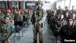 FILE - Afghan National Army soldiers attend their graduation ceremony while a NATO soldier stands guard at the Kabul Military Training Centre in Kabul, Afghanistan, Jan. 27, 2019.