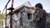 FILE - A man smokes near a residential building, which locals said was damaged during recent shelling, in Donetsk, Ukraine, Aug. 7, 2015. 