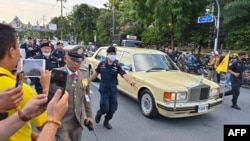 Police escort the limousine carrying Thailand's Queen Suthida and Prince Dipangkorn Rasmijoti as royalist supporters take photos of the the royal motorcade in Bangkok on October 14, 2020. (Photo by Mladen ANTONOV / AFP)