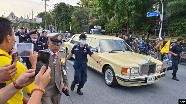 Police escort the limousine carrying Thailand's Queen Suthida and Prince Dipangkorn Rasmijoti as royalist supporters take photos of the the royal motorcade in Bangkok on October 14, 2020. (Photo by Mladen ANTONOV / AFP)