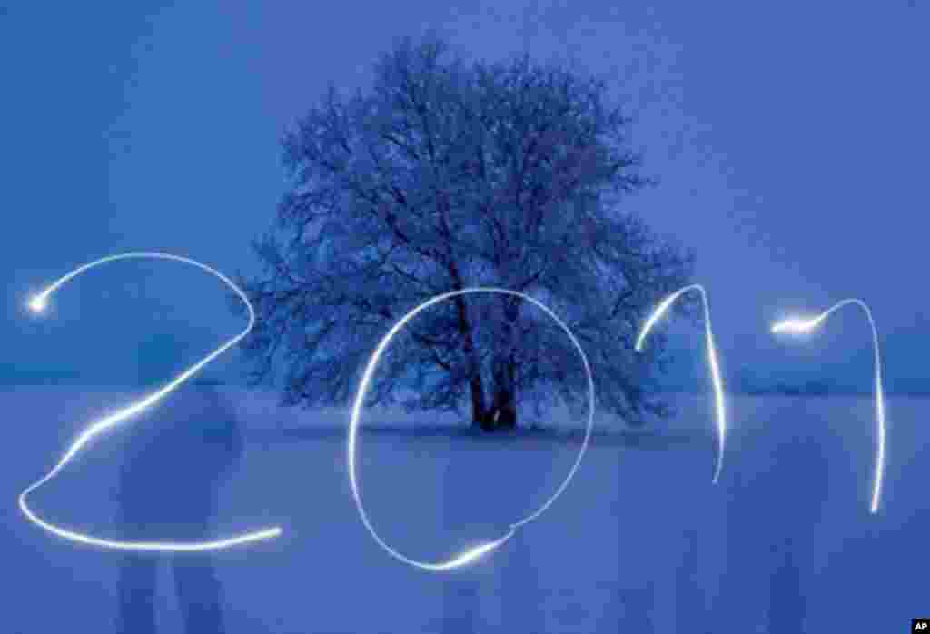 A man writing "2011" with a torch into the blue evening sky on a snow covered field in Sieversdorf, eastern Germany, 30 Dec 2010. (AFP Image)