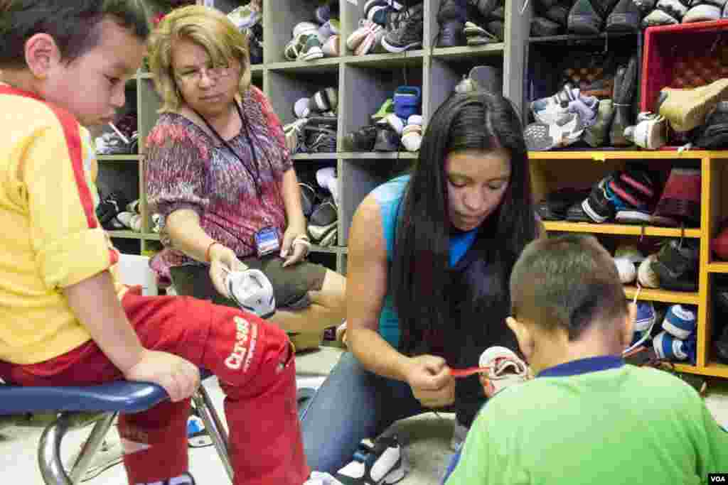 Volunteer Blanca Bermudez helps newly-arrived migrant Ana and her sons choose new shoes from the donations at the Holding Institute in Laredo, Texas, Aug. 12, 2014. (VOA / V. Macchi)