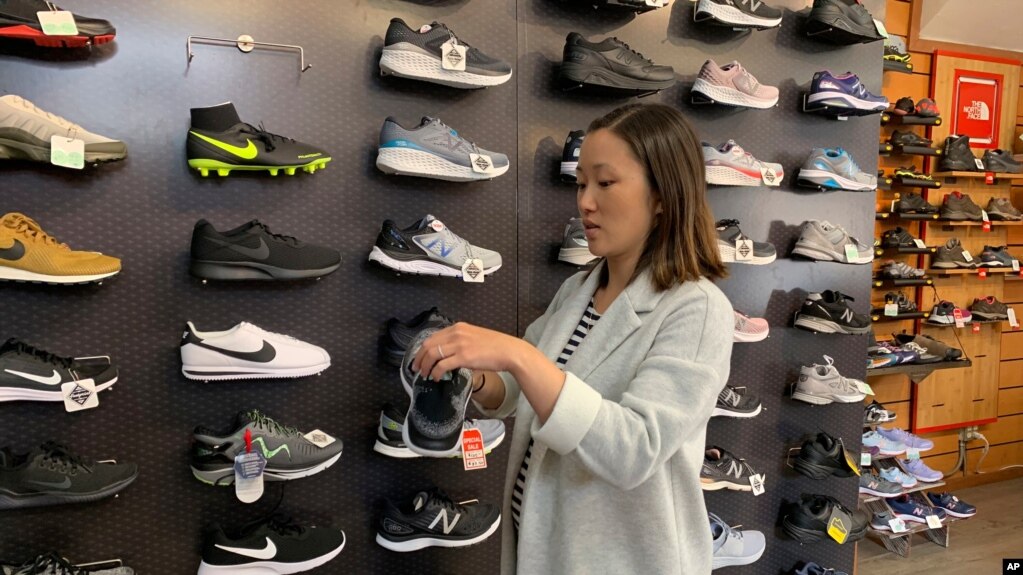 在这张2019年8月28日拍摄的照片中，家人在旧金山拥有 Footprint 鞋店的詹妮弗·李 (Jennifer Lee) 站在一堵运动鞋的墙边，其中许多运动鞋是中国制造的。(photo:VOA)