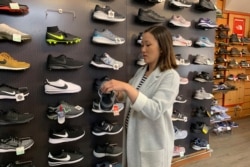 Jennifer Lee, whose family owns Footprint shoe store in San Francisco, stands by a wall of athletic shoes, Aug. 28, 2019. Many of the shoes are made in China and will be subject to new U.S. tariffs on Chinese goods starting Sept. 1.