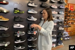 FILE - Jennifer Lee, whose family owns Footprint shoe store in San Francisco, stands by a wall of athletic shoes, many of which are made in China and are subject to U.S. tariffs on Chinese goods, Aug. 28, 2019.