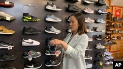 在这张2019年8月28日拍摄的照片中，家人在旧金山拥有 Footprint 鞋店的詹妮弗·李 (Jennifer Lee) 站在一堵运动鞋的墙边，其中许多运动鞋是中国制造的。