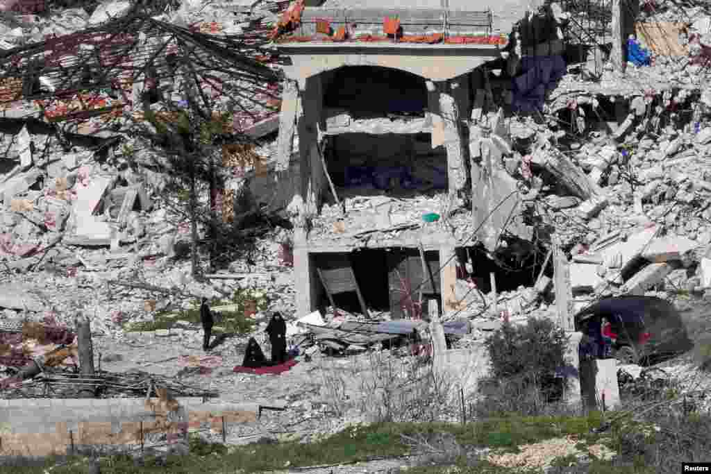 Women pray next to the rubble of destroyed houses, on the Lebanese side of the Israel-Lebanon border near the village of Adaisseh, as seen from the Israeli.