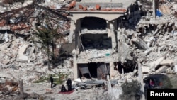 Women pray next to the wreckage of destroyed houses, on the Lebanese side of the Israel-Lebanon border near the village of Adaisseh, as seen from the Israeli.