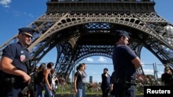 FILE - French CRS policemen patrol as tourists walk past in front of the Eiffel Tower in Paris, Aug. 20, 2016. 