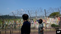 Visitors wearing face masks as a precaution against the coronavirus, walk near the barbed-wire fences decorated with ribbons written with messages wishing for the reunification of the two Koreas at the Imjingak Pavilion in Paju, South Korea,…