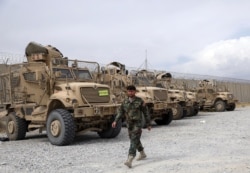 FILE - An Afghan army soldier walks past Mine Resistant Ambush Protected vehicles, MRAP, that were left after the American military left Bagram air base, in Parwan province north of Kabul, Afghanistan, July 5, 2021.