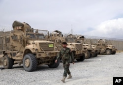 FILE - An Afghan army soldier walks past Mine Resistant Ambush Protected vehicles, MRAP, that were left after the American military left Bagram air base, in Parwan province north of Kabul, Afghanistan, July 5, 2021.