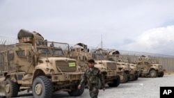An Afghan army soldier walks past Mine Resistant Ambush Protected vehicles, MRAP, that were left after the American military left Bagram air base, in Parwan province north of Kabul, Afghanistan, July 5, 2021.