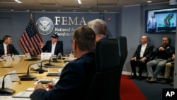 ປະທານາທິບໍດີ ທຣຳ, ຊ້າຍ, ຟັງໃນຂະນະທີ່ ທ່ານແກຣມ (Graham), ຜູ້ອຳນວຍການ ອົງການ NOAA's National Hurricane Center,ຢູ່ໃນຈໍໂລລະພາບ, ລາຍງານຄວາມຄືບໜ້າ ໃນລະຫວ່າງ ກອງປະຊຸມແຈ້ງໃຫ້ຊາບໂດຍຫຍໍ້ ກ່ຽວກັບ ພາຍຸເຮີຣິເຄນໂດຣຽນ ຢູ່ທີ່ Federal Emergency Management Agency (FEMA), ວັນອາທິດ ທີ 1 ກັນຍາ 2019.