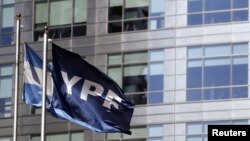 Bendera perusahaan gas dan minyak YPF berkibar di samping bendera Argentina di luar kantor pusat YPF di Buenos Aires. (Foto: Reuters)