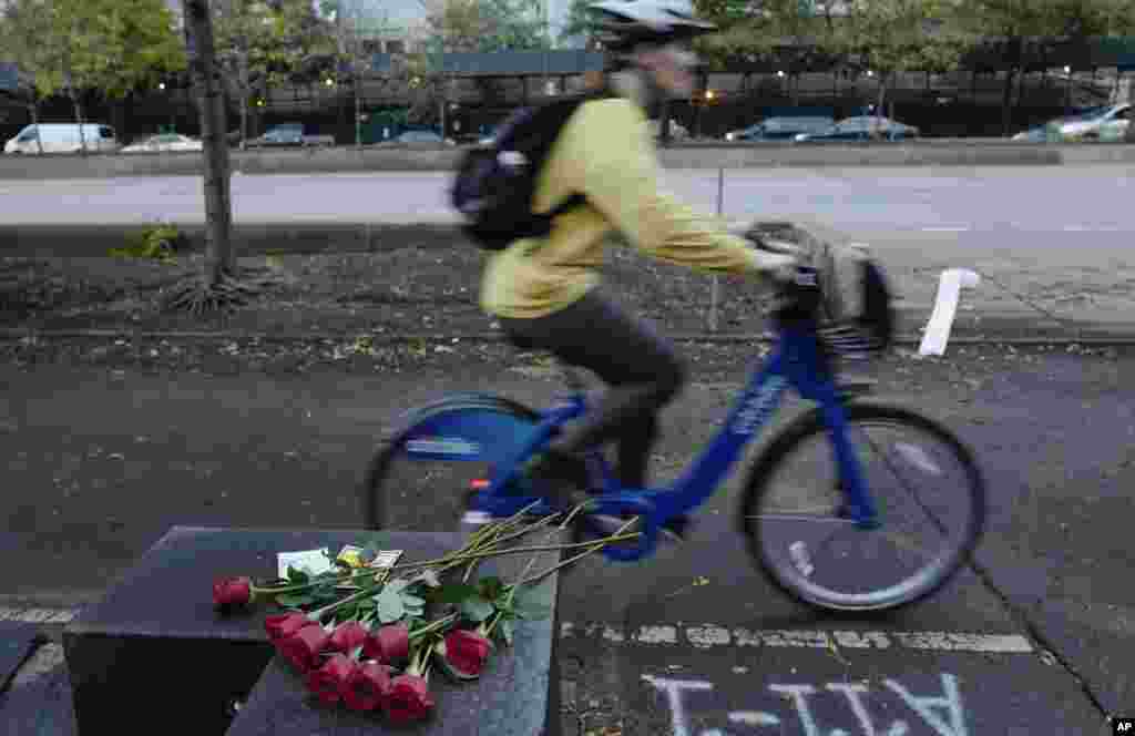 A bicyclist passes flowers left in honor of the victims of a nearby bike path attack in New York.