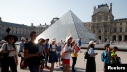 2018年7月26日，在法国巴黎卢浮宫外，中国游客站在金字塔前，这座金字塔是在中国出生的美国建筑师贝聿铭设计的。