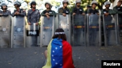 Una niña cubierta con la bandera de Venezuela se sienta en protesta frente a fuerzas de seguridad que bloquean el acceso a la morgue en Caracas de partidarios y dolientes del ex efectivo de seguridad Óscar Pérez, que se rebeló contra el gobierno del presidente Nicolás Maduro. Enero 20 de 2018.