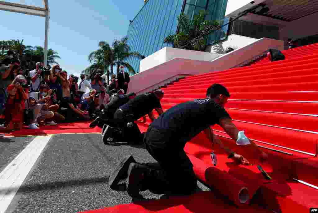 Photographers and cameramen watch as workers install the red carpet in front of the main entrance of the Festival Palace before the opening ceremony of the 74th Cannes Film Festival in Cannes, France.