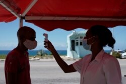 Seorang dokter mengecek suhu seorang pria yang meninggalkan Provinsi Havana di pos pemeriksaan di Boca de Jaruco, Kuba, di tengah pandemi virus corona, Senin, 10 Agustus 2020.(Foto: Reuters)