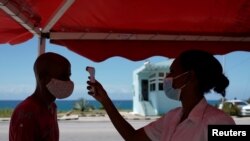 Seorang dokter mengecek suhu seorang pria yang meninggalkan Provinsi Havana di pos pemeriksaan di Boca de Jaruco, Kuba, di tengah pandemi virus corona, Senin, 10 Agustus 2020.(Foto: Reuters)