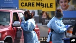 အမေရိကန် ဆေးရုံတခုအနီး ယာဉ်မောင်းအား ကိုရိုနာဗိုင်းရပ်စ် ရှိမရှိ စမ်းသပ်စစ်ဆေးနေသည့် ကျန်းမာရေးဝန်ထမ်းများ။ (မတ် ၂၀၊ ၂၀၂၀)