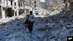  FILE - A Syrian man holds a girl as he stands on the rubble of houses that were destroyed by Syrian government forces air strikes in Aleppo, Syria, on April 21, 2014. The French foreign minister says Russia could face war crimes for its bombing campaign of Aleppo.