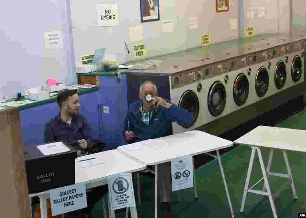 A presiding officer (R) and poll clerk wait for early morning voters at a polling station set up in a launderette and nail bar in Headington outside Oxford, west of London as Britain holds a general election.