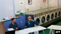 A presiding officer (R) and poll clerk wait for early morning voters at a Polling Station set up in a launderette and nail bar in Headington outside Oxford, west of London, on June 8, 2017, as Britain holds a general election. 