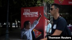 People walk past a poster depicting Greek Prime Minister Alexis Tsipras at the election kiosk of the leftist Syriza party in Athens, July 6, 2019. The slogan on the poster reads, "Now we decide for our lives."