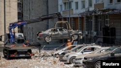 Pegawai dinas kota memindahkan mobil yang hancur dari tempat parkir di sebelah gedung apartemen yang rusak berat selama serangan drone Rusia besar-besaran, di tengah serangan Rusia terhadap Ukraina, di Kyiv, Ukraina 30 Mei 2023. (Foto: REUTERS/Alina Smutko)