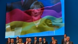 In this Wednesday, Dec. 7, 2016 file photo, the CDU board sings the national anthem in front of a screen showing German chancellor Angela Merkel on the national flag at the general party conference of the Christian Democratic Union, CDU, in Essen, Germany