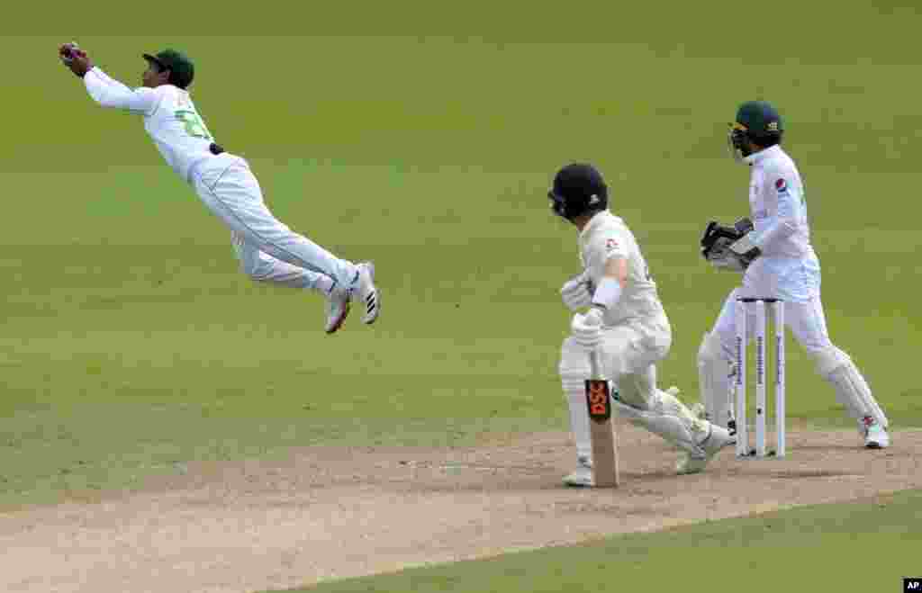 Pakistan&#39;s Asad Shafiq, left, dives to catch the ball to dismiss England&#39;s Dominic Bess, center, during the third day of the first cricket test match between England and Pakistan at Old Trafford in Manchester, England.