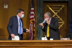 Senate Intelligence Committee Chairman Sen. Richard Burr, right, adjusts his mask while talking to Vice Chairman Sen. Mark Warner, at a hearing to consider Rep. John Ratcliffe to be Director of National Intelligence, May 5, 2020.