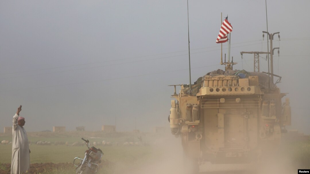 FILE - A man gestures at U.S military vehicles driving in the town of Darbasiya next to the Turkish border, Syria, April 28, 2017. 