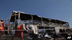 Para pekerja membersihkan puing-puing pasca kecelakaan bus yang menabrak pembatas jalan dan terbakar, di Mehabubnagar, Andhra Pradesh, India (30/10).