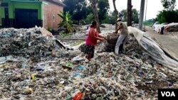 Supiati dan Saji mengangkut sampah plastik impor di pekarangan mereka di Mojokerto, Jawa Timur, untuk kemudian disortir dan dijual kembali (foto: Petrus Riski/VOA).