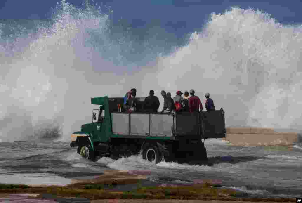 A dump truck carrying cleaning workers drives on Havana&#39;s Malecón as a wave crashes on the sea wall, in Cuba.