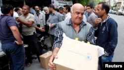 FILE - Displaced Syrians collect rations provided by the World Food Program in front of a distribution center in Damascus, Oct. 19, 2014.