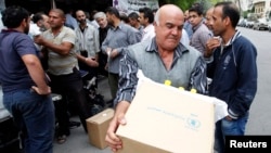 FILE - Displaced Syrians collect rations provided by the World Food Program in front of a distribution center in Damascus, Oct. 19, 2014.