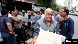 FILE - Displaced Syrians collect rations provided by the World Food Program in front of a distribution center in Damascus, Oct. 19, 2014.