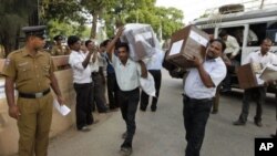 Police stand guard, left, as Sri Lankan polling officials carry ballot boxes to a counting center in Jaffna, Sri Lanka, July 23, 2011