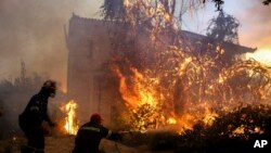 Firefighters try to extinguish flames outside a house in Agrilitsa village on the Greek island of Evia, Aug. 13, 2019.