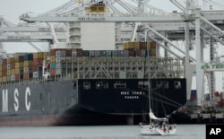 FILE - A sailboat makes its way past the container ship MSC Ivana as she is unloaded at the Port of Oakland in Oakland, California, March 3, 2016.