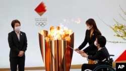 Tokyo 2020 President Seiko Hashimoto, left, watches Japanese actress Satomi Ishihara and Paralympian Aki Taguchi light the celebration cauldron on the first day of the Tokyo 2020 Olympic torch relay in Naraha, Fukushima prefecture, northeastern Japan, Thu