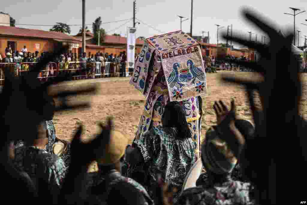 An Egungun, a visible manifestation of the spirits of departed ancestors who periodically revisit the human community for remembrance, dances as musicians cheer in Ouidah, Benin, during the first day of the Voodoo Festival.