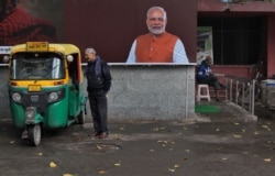 FILE - A man chats with an auto rickshaw driver standing next to a portrait of Indian Prime Minister Narendra Modi outside a public toilet in New Delhi, India, Feb. 14, 2019.