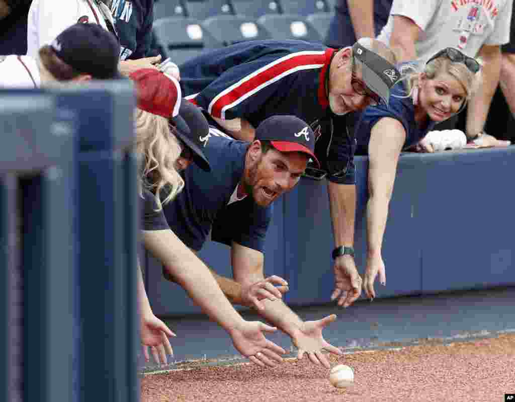 Fans reach over a baseball rolled to them by Atlanta Braves coaches as the team takes batting practice before a spring training baseball game against the Washington Nationals in West Palm Beach, Florida.