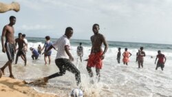 Des jeunes jouent au football devant d'autres se baignant dans la mer sur une plage de Grand-Bassam, en Côte d'Ivoire, le 28 mars 2021.